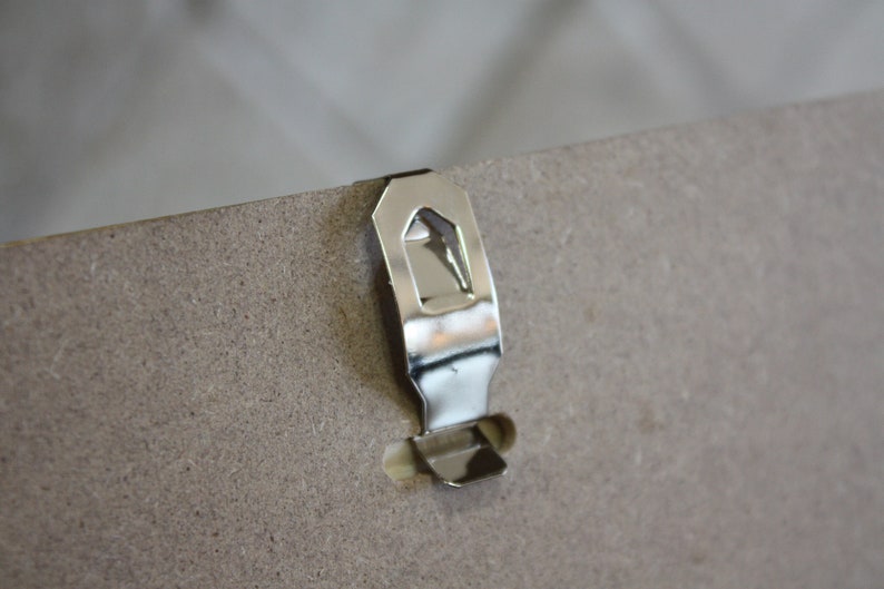 May include: A silver metal hanging hook attached to the back of a picture frame.
