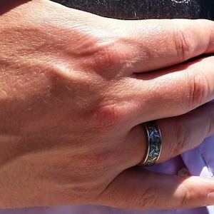 May include: A close-up of a hand wearing a silver ring with a black and white patterned design.