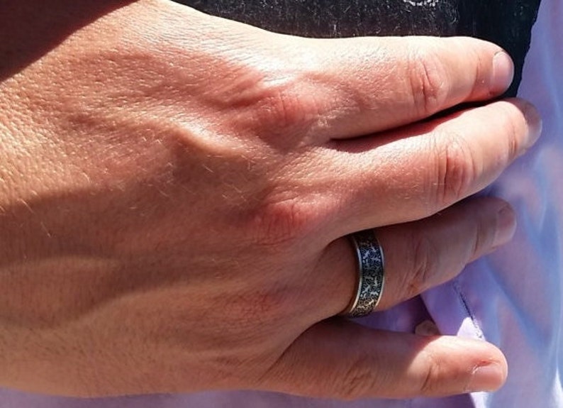 May include: A close-up of a hand wearing a silver ring with a black and white patterned design.