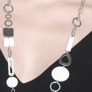 May include: A silver chain necklace with white and silver geometric shapes. The necklace features a variety of shapes, including circles, squares, and ovals.