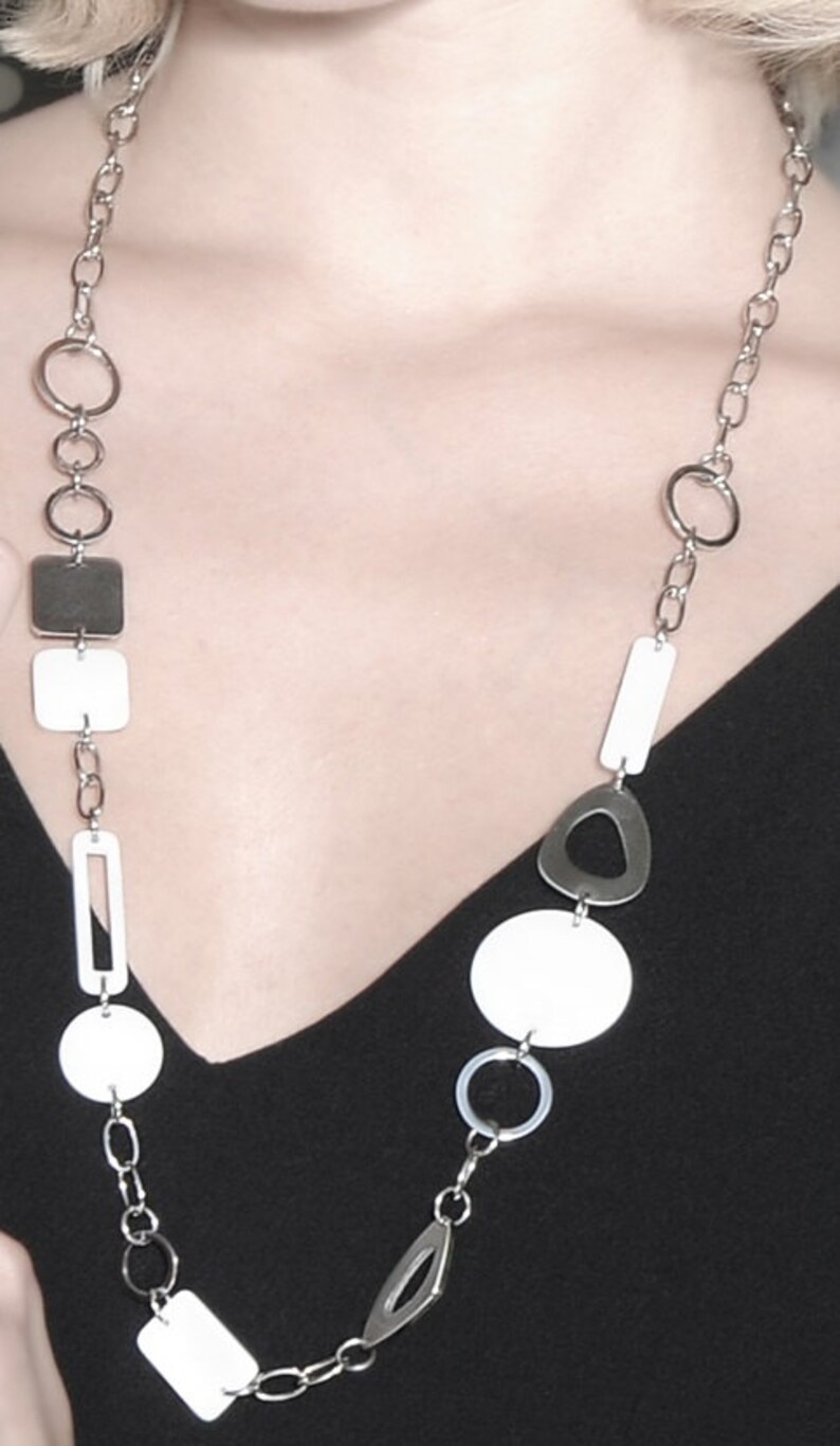 May include: A silver chain necklace with white and silver geometric shapes. The necklace features a variety of shapes, including circles, squares, and ovals.