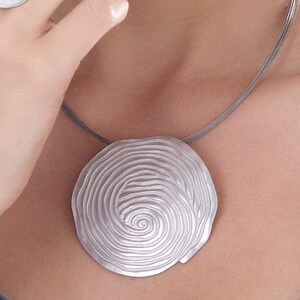 May include: A silver necklace with a large, round pendant featuring a spiral design. The pendant is made of metal and has a smooth, polished finish.