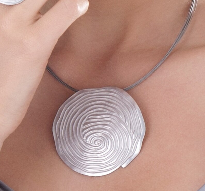 May include: A silver necklace with a large, round pendant featuring a spiral design. The pendant is made of metal and has a smooth, polished finish.