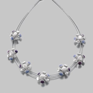May include: A silver necklace with a double strand of chain and multiple clusters of white, blue, and purple stones.