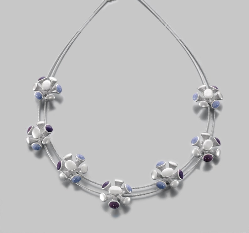 May include: A silver necklace with a double strand of chain and multiple clusters of white, blue, and purple stones.