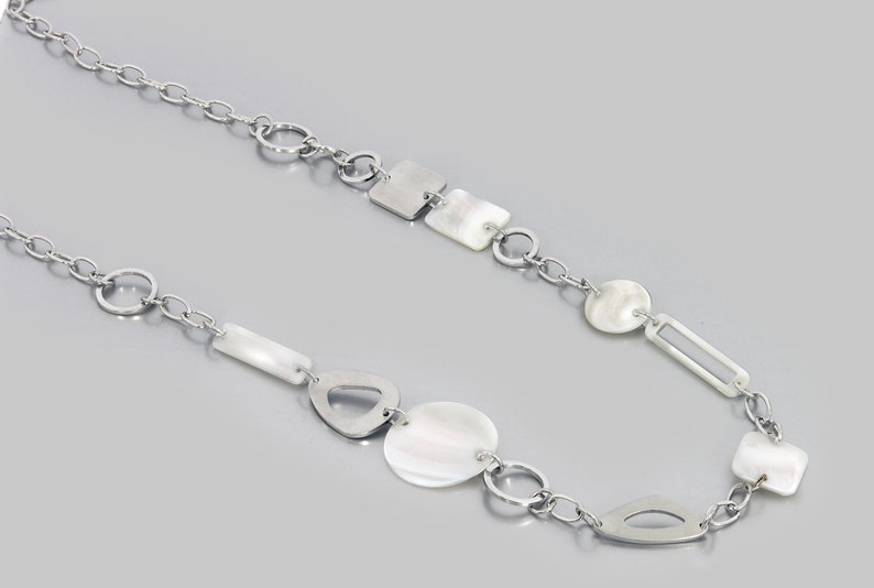 May include: A silver chain necklace with white shell and metal geometric shapes. The necklace features a variety of shapes, including circles, squares, rectangles, and ovals.