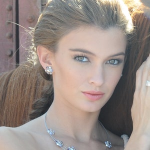 May include: A woman with long, light brown hair is wearing a silver necklace with purple stones. The necklace has a delicate, layered design.