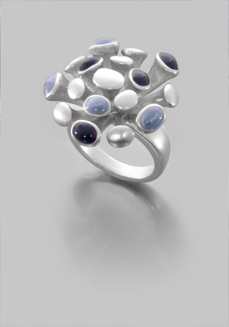 May include: A silver ring with a cluster of blue, white, and purple stones. The stones are set in a silver band and are arranged in a flower-like pattern.