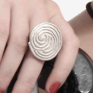 May include: A silver ring with a spiral design. The ring is round and has a textured surface.