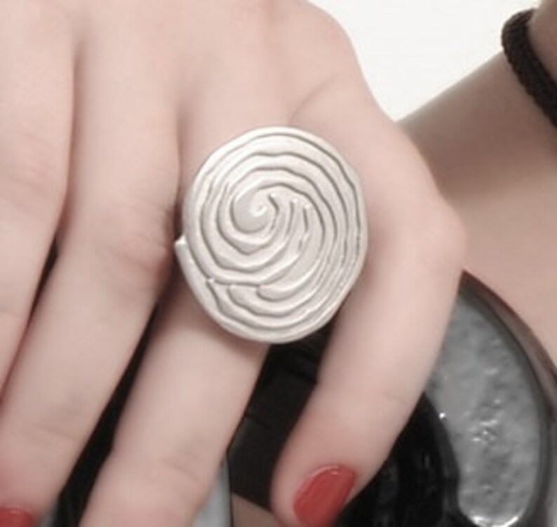 May include: A silver ring with a spiral design. The ring is round and has a textured surface.