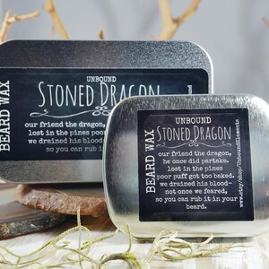 May include: Two silver tins with black labels that read "Unbound Stoned Dragon Beard Wax". The text on the labels describes a dragon who got too baked and had his blood drained.
