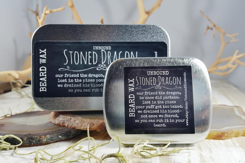May include: Two silver tins with black labels that read "Unbound Stoned Dragon Beard Wax". The text on the labels describes a dragon who got too baked and had his blood drained.