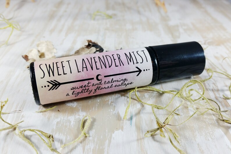 Puede incluir: Un frasco negro con rodillo y una etiqueta blanca que dice "SWEET LAVENDER MIST" con un gr&aacute;fico de luna creciente y flecha. La etiqueta tambi&eacute;n dice "sweet and calming, a lightly floral escape."