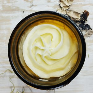 May include: A close-up of a glass jar filled with a swirl of white body butter.