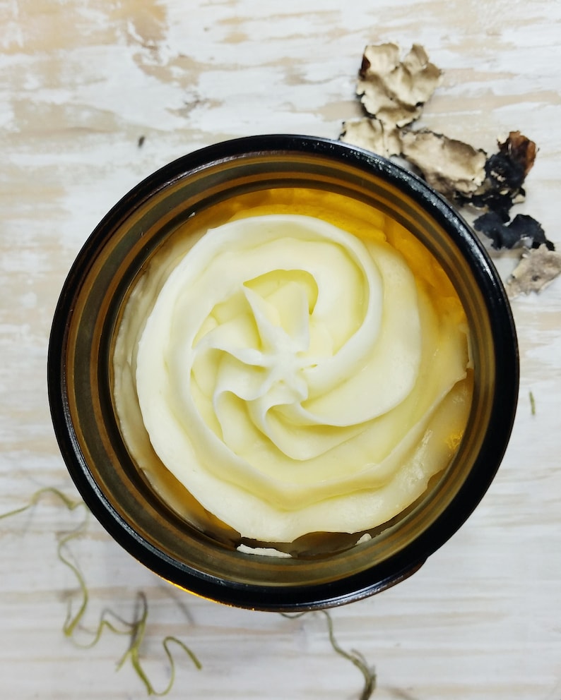 May include: A close-up of a glass jar filled with a swirl of white body butter.
