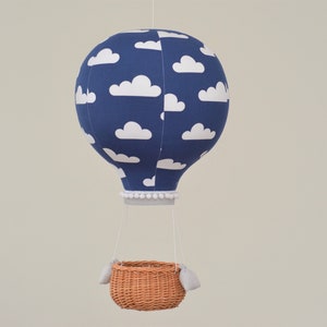 Hot air balloon hangs on a string. It is made of several panels of fabric, filled and has round shape. Bottom finished with a ribbon. Wicker basket with sand bags is attached under the balloon