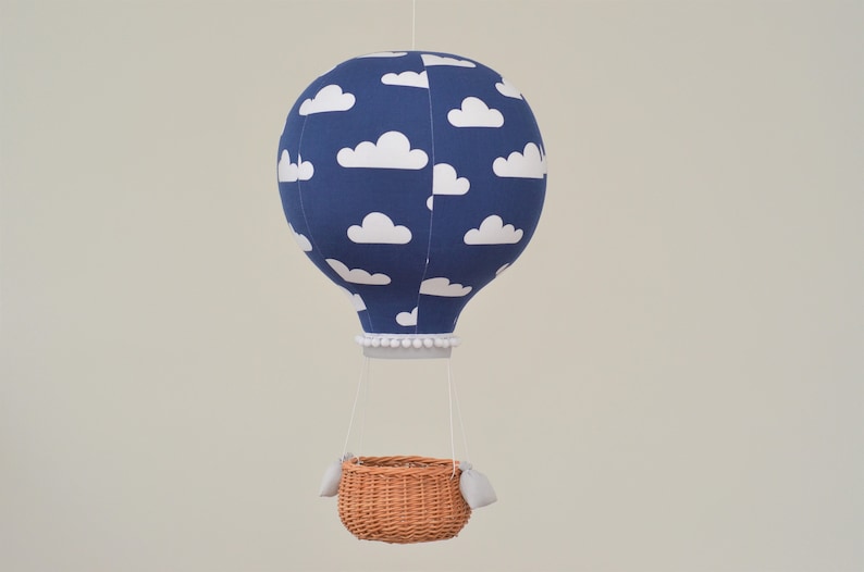 Hot air balloon hangs on a string. It is made of several panels of fabric, filled and has round shape. Bottom finished with a ribbon. Wicker basket with sand bags is attached under the balloon