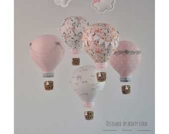 May include: A pink, white, and gray baby mobile with four hot air balloons. Each balloon has a different pattern and is decorated with lace and a small basket.