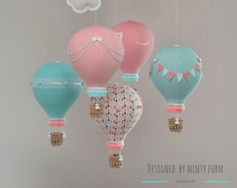 May include: A baby mobile with five hot air balloons in pink, blue, and white with polka dots, stripes, and a heart pattern. The balloons are suspended from a white cloud.