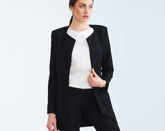May include: A black blazer with a collarless neckline and a white blouse underneath. The blazer has a long, fitted silhouette and a slightly flared hem.