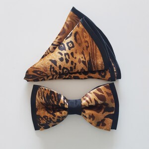 May include: A brown and black bow tie with a leopard print pattern. The bow tie is made of satin and has a black trim.