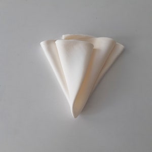 Puede incluir: Una servilleta de tela blanca doblada en forma triangular.