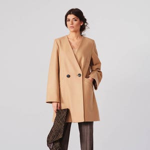 May include: A camel-colored double-breasted coat with a v-neck and long sleeves. The coat has two pockets and a button closure.