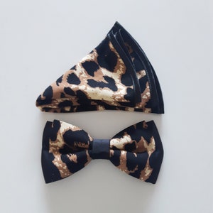 May include: A brown and black bow tie with a leopard print pattern. The bow tie is made of fabric and has a black satin trim.
