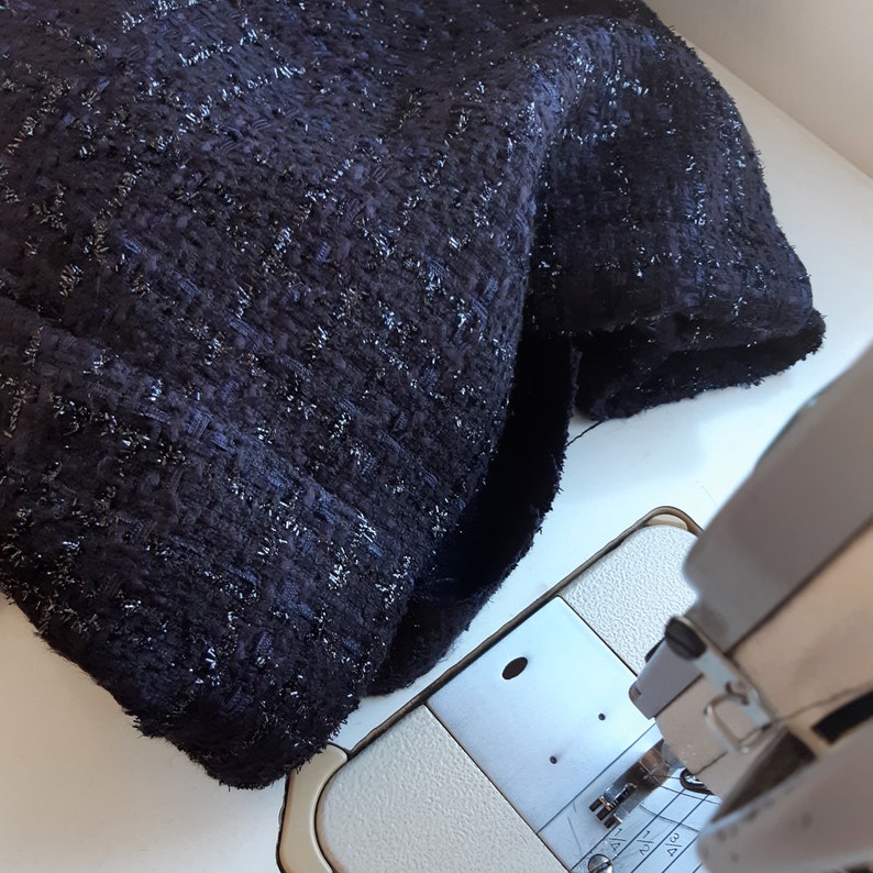 May include: Close-up of a dark blue fabric with a textured, sparkly finish. The fabric is being fed into a sewing machine.