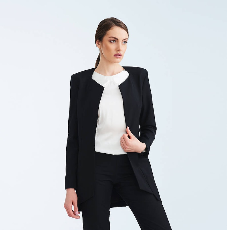 May include: A black blazer with a collarless neckline and a white blouse underneath. The blazer has a long, fitted silhouette and a slightly flared hem.