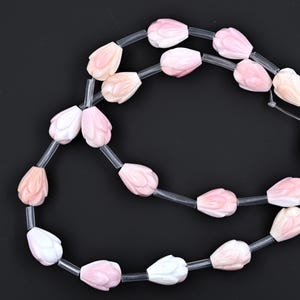 Puede incluir: Una hebra de cuentas de concha rosa y blanca en forma de lágrima. Las cuentas están enhebradas en un cordón elástico transparente.