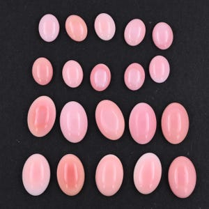 May include: A collection of twenty oval-shaped pink cabochons arranged in four rows. Each gemstone features a smooth, polished surface with a consistent light pink hue and a rounded, domed top, displaying a uniform appearance across all pieces.