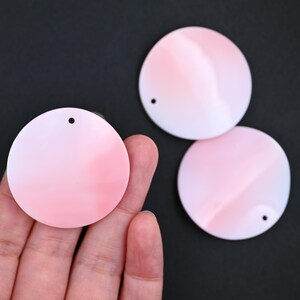 May include: Three circular flat pendants featuring a smooth gradient transition from soft white to pale pink. Each disc has a single small circular hole punched near the top edge for attachment, showcasing a clean, polished surface finish.