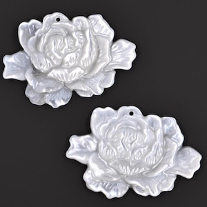 May include: Two white, pearl-like, flower-shaped pendants with a hole at the top for stringing. The flowers have a raised, textured design.