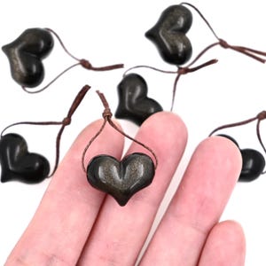 Puede incluir: Seis colgantes de coraz&oacute;n negro con motas doradas, cada uno en un cord&oacute;n marr&oacute;n.