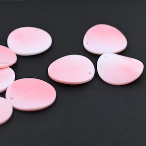 Puede incluir: Varias cuentas ovaladas rosas y blancas con un agujero en la parte superior. Las cuentas tienen un acabado liso y brillante y están dispuestas sobre un fondo oscuro. Adecuadas para la creación de joyas.