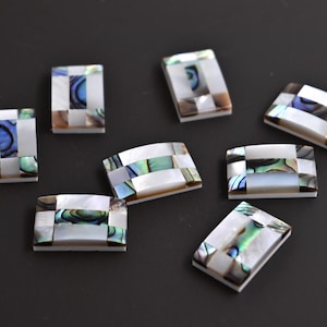 以下が含まれることがあります： 市松模様の虹色のアワビ貝のタイルが8枚。タイルは白で、青、緑、茶色のアクセントが付けられています。