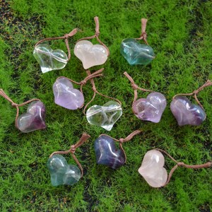 May include: Assortment of heart-shaped crystal pendants in various colors, including clear, pink, purple, and green. Each pendant is strung on a brown cord.
