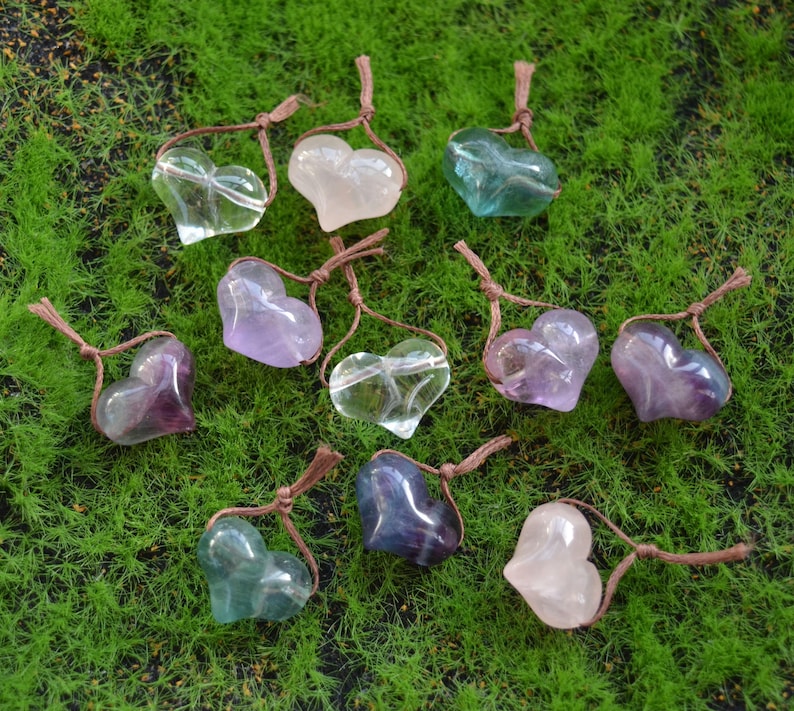 May include: Assortment of heart-shaped crystal pendants in various colors, including clear, pink, purple, and green. Each pendant is strung on a brown cord.