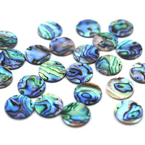 Könnte beinhalten: Eine Sammlung kreisförmiger Abalone-Muschelscheiben mit irisierenden Mustern in Blau, Grün und Violett. Jedes flache, runde Stück weist eine einzigartige, wirbelnde natürliche Textur mit polierter Oberfläche und einem kleinen Loch auf.