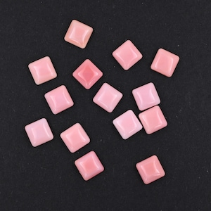 May include: A collection of thirteen small, square-shaped tiles with a smooth, glossy finish in a soft pastel pink colour. Each tile features slightly rounded edges and a raised, beveled centre, creating a uniform appearance across the set.