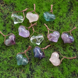May include: Ten heart-shaped crystal pendants with brown cords. The crystals are in various colors, including purple, pink, green, and blue.