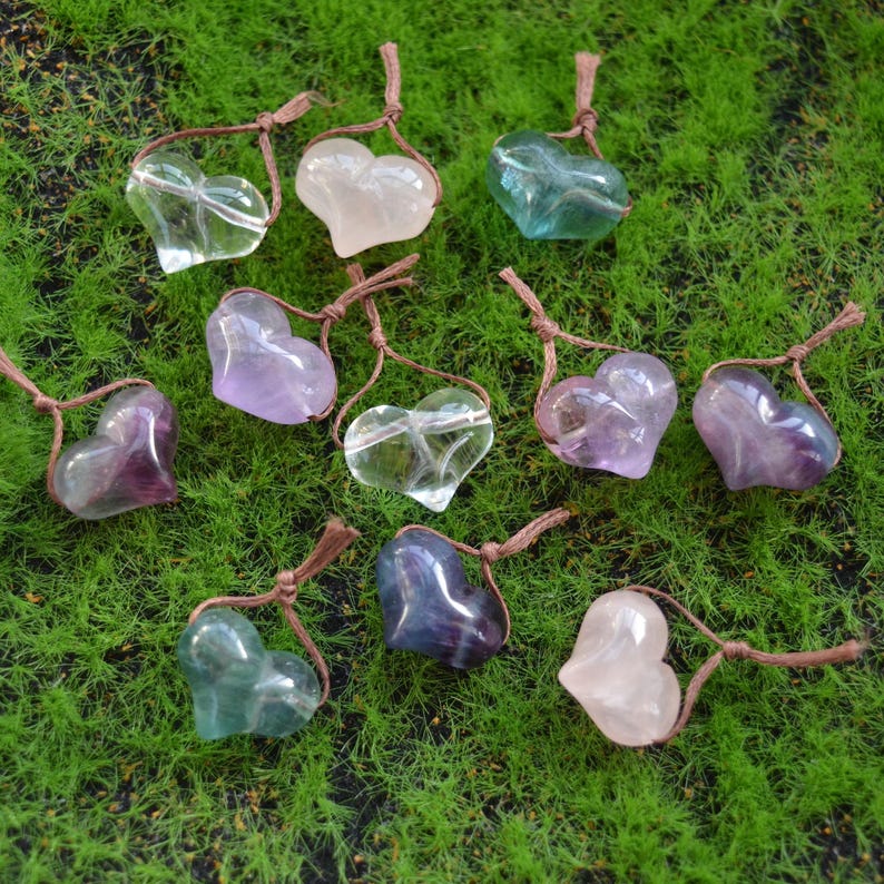 May include: Ten heart-shaped crystal pendants with brown cords. The crystals are in various colors, including purple, pink, green, and blue.