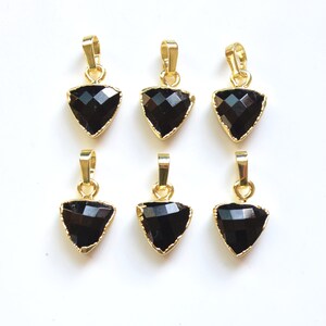 May include: Six black triangle-shaped pendants with gold-toned metal settings. The pendants are faceted and have a shiny finish.