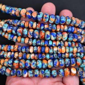 May include: A strand of round, flat-disc shaped beads featuring a marbled pattern of vibrant royal blue, bright orange, and turquoise colors. The beads are arranged in multiple rows, showcasing a smooth, polished finish with intricate color variations.