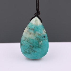 May include: A turquoise and white marbled teardrop pendant, suspended from a dark brown cord. The gemstone's polished surface displays natural variations. The pendant is a striking piece of jewellery, with a unique, organic design.