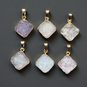 Puede incluir: Seis colgantes de oro con piedras de cristal de diferentes colores. Los colgantes tienen forma cuadrada con esquinas redondeadas. Las piedras son todas de diferentes tonos de morado y blanco.