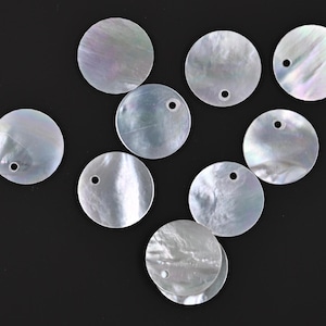 May include: Ten white iridescent round shell discs with a small hole in the center. The discs are arranged in a random pattern on a black background.