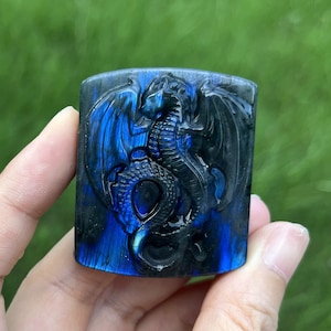 Peut inclure: Une pierre précieuse en labradorite bleue et noire sculptée avec un motif de dragon. La pierre précieuse a un éclat iridescent.