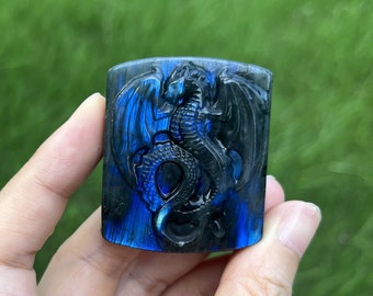 May include: A blue and black labradorite gemstone carved with a dragon design. The gemstone has an iridescent sheen.